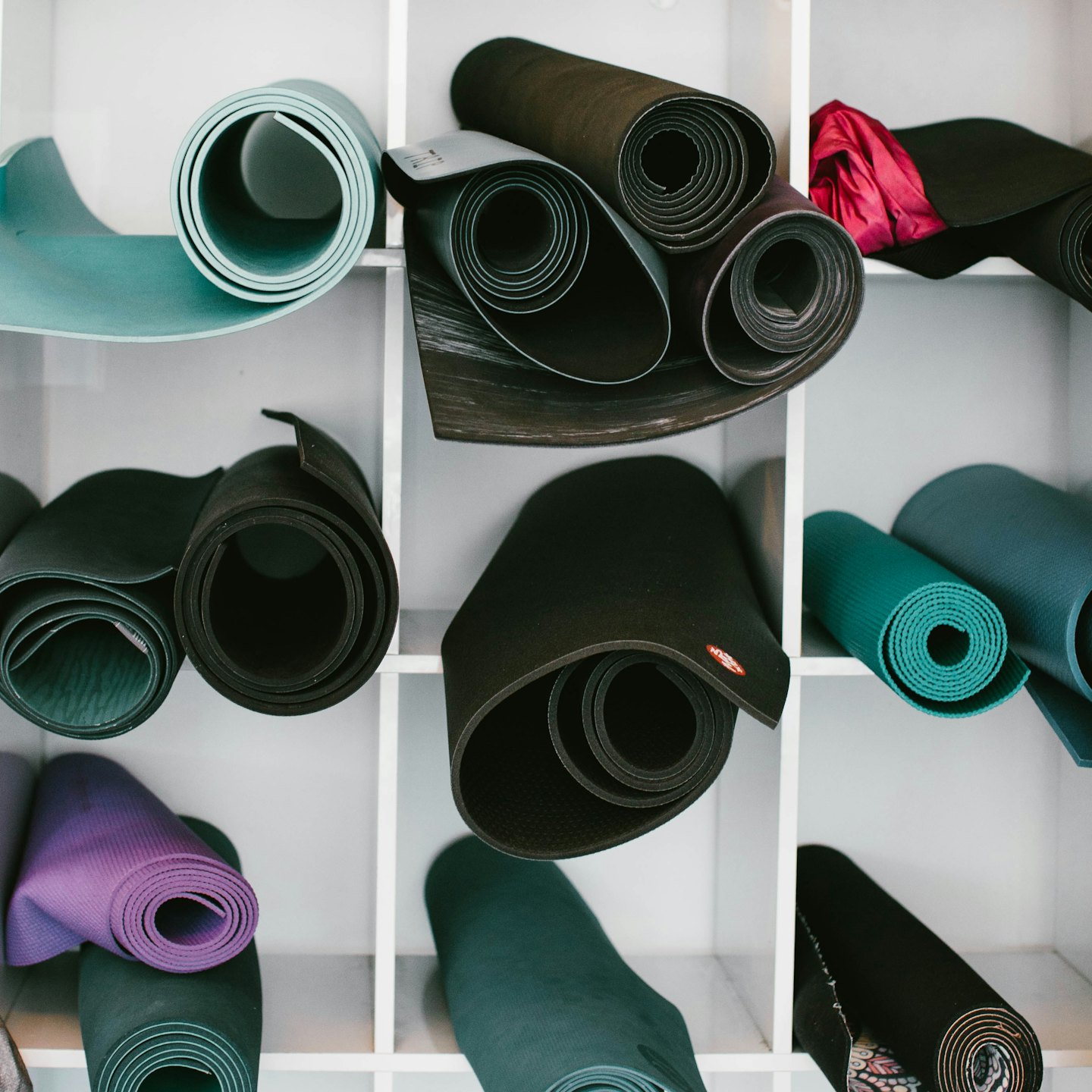 Rolled yoga mats in various colors neatly stored in cubbies.