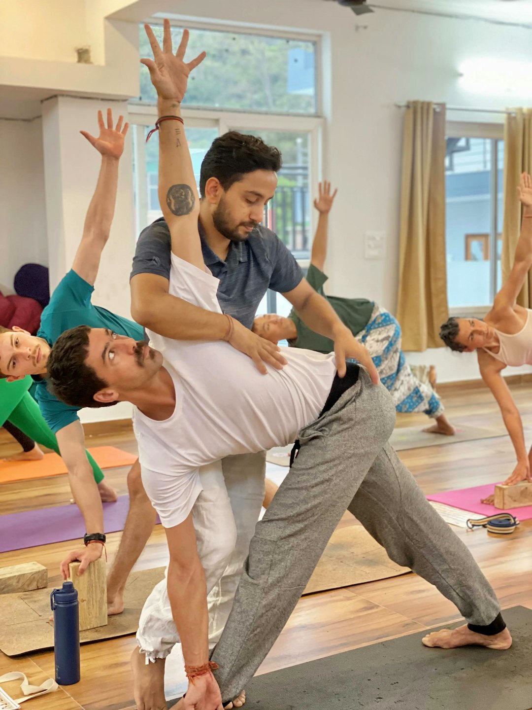 Yoga instructor helps student adjust pose in bright studio.