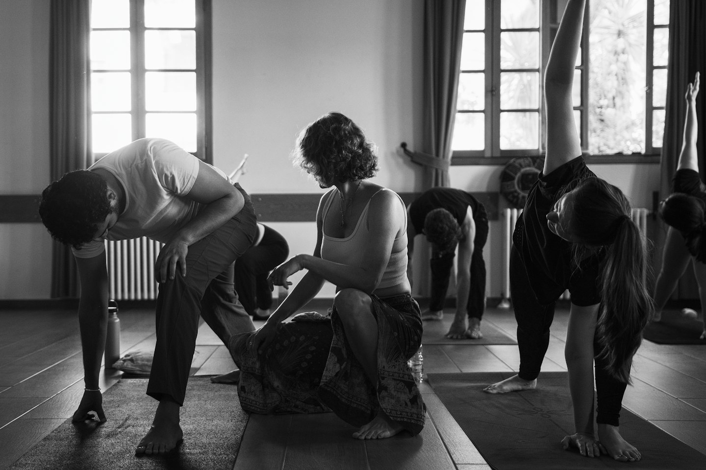 Adults practice yoga poses on mats in a sunlit studio.
